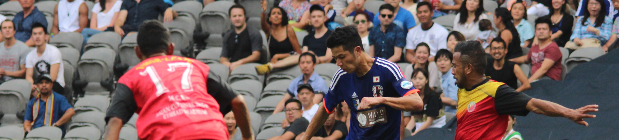 Community footballers competing in front of a diverse Melbourne crowd.